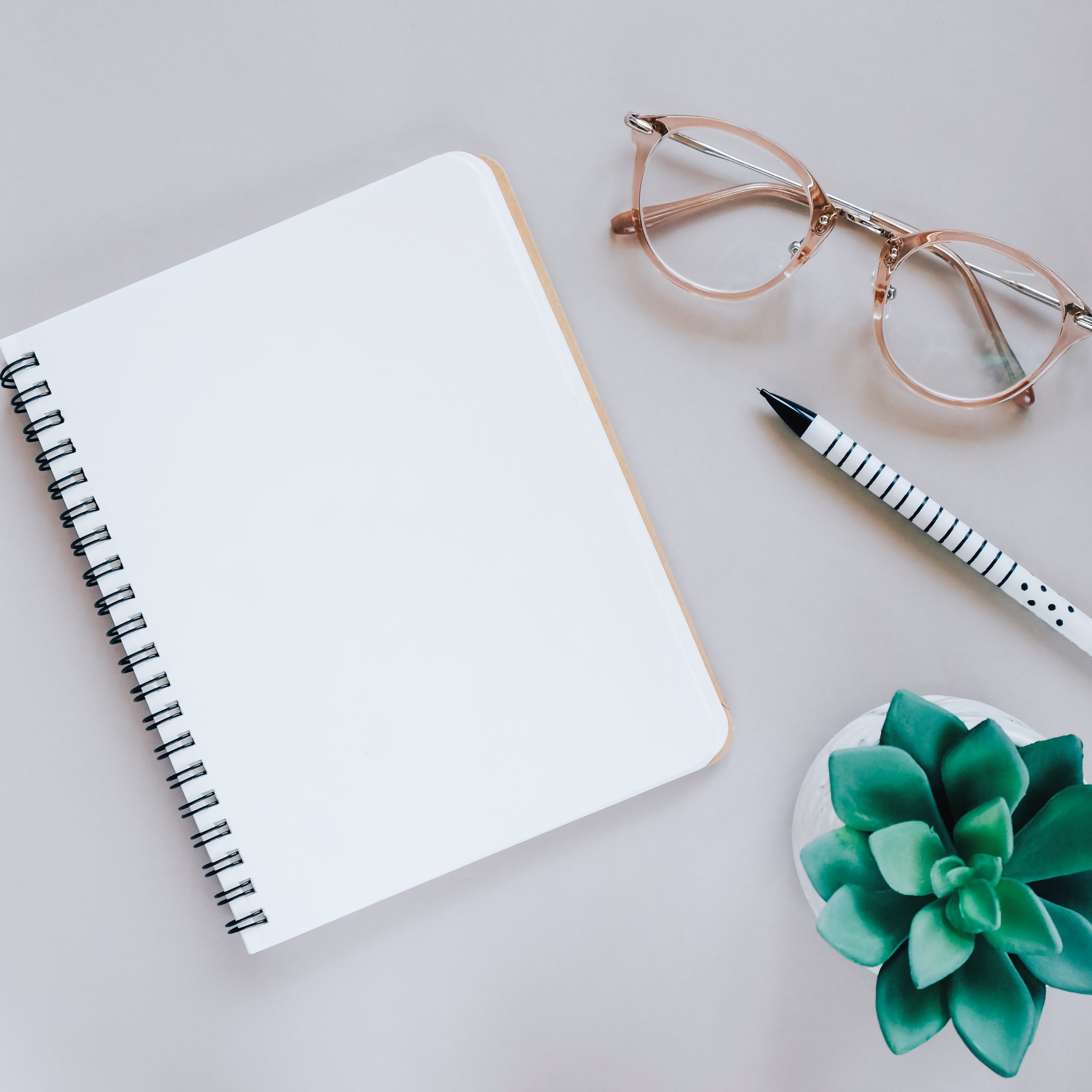 Flat lay of minimal workspace desk with notebook, eyeglasses and work